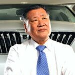 En man i kostym sitter bredvid en bil. (AI text)