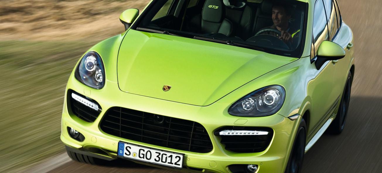 En grönt Porsche Cayenne kör nedför en landsväg. (AI text)