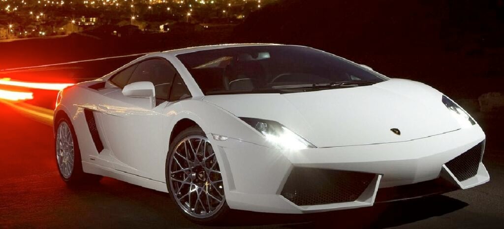 En vit sportbil kör nerför en stadsgata på natten. (AI text)