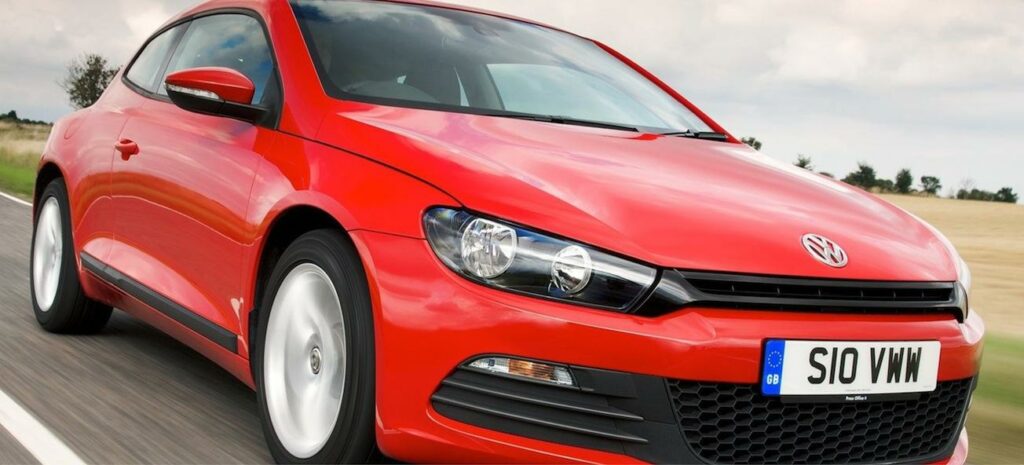 En röd Volkswagen Golf kör nedför en landsväg. (AI text)