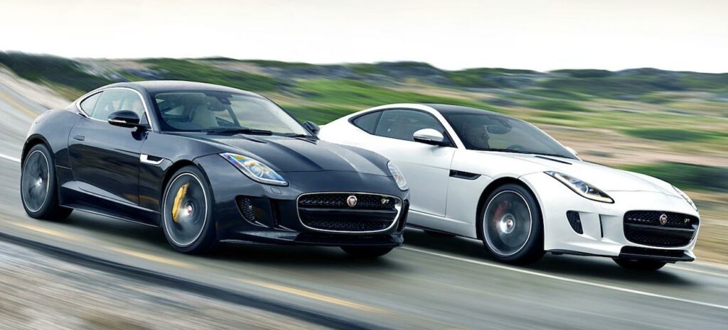 Två Jaguar-bilar kör längs en väg. (AI text)