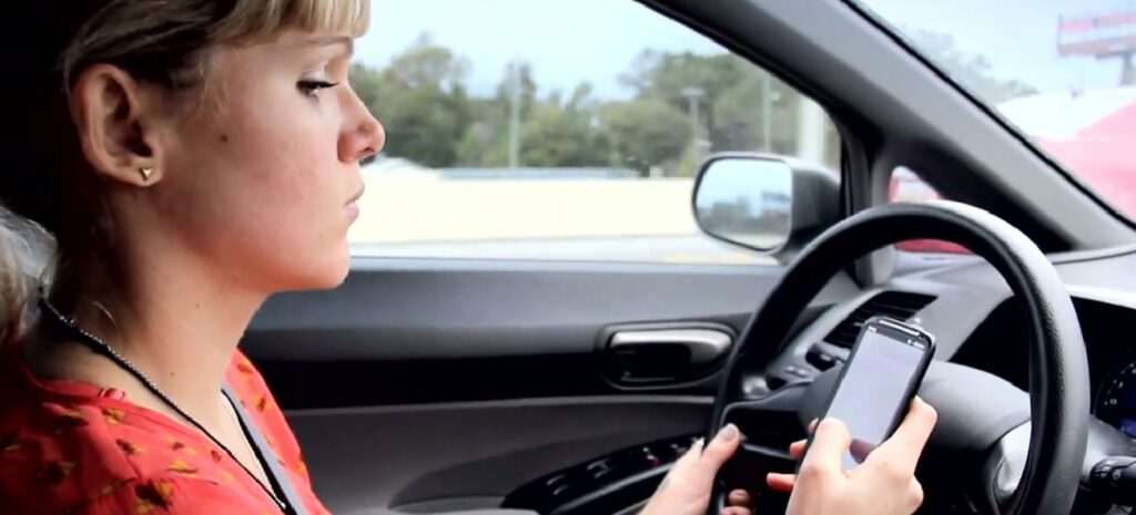En kvinna kör en bil samtidigt som hon använder sin telefon. (AI text)