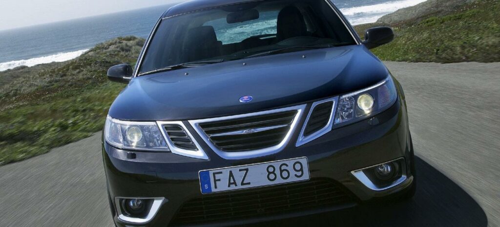 En svart bil kör nerför en väg nära havet. (AI text)