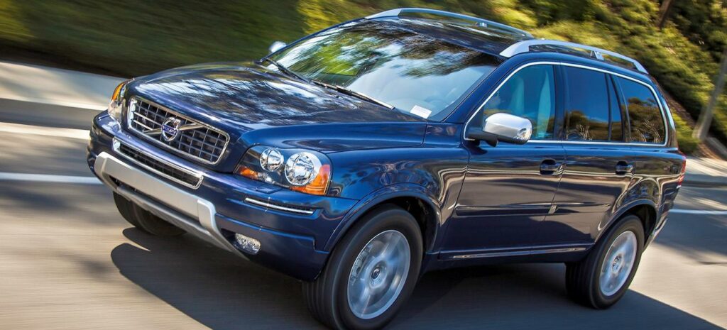 En blå Volvo XC90 kör längs en landsväg. (AI text)