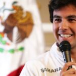 En man i vit skjorta ler och håller ett mikrofon. (AI text)