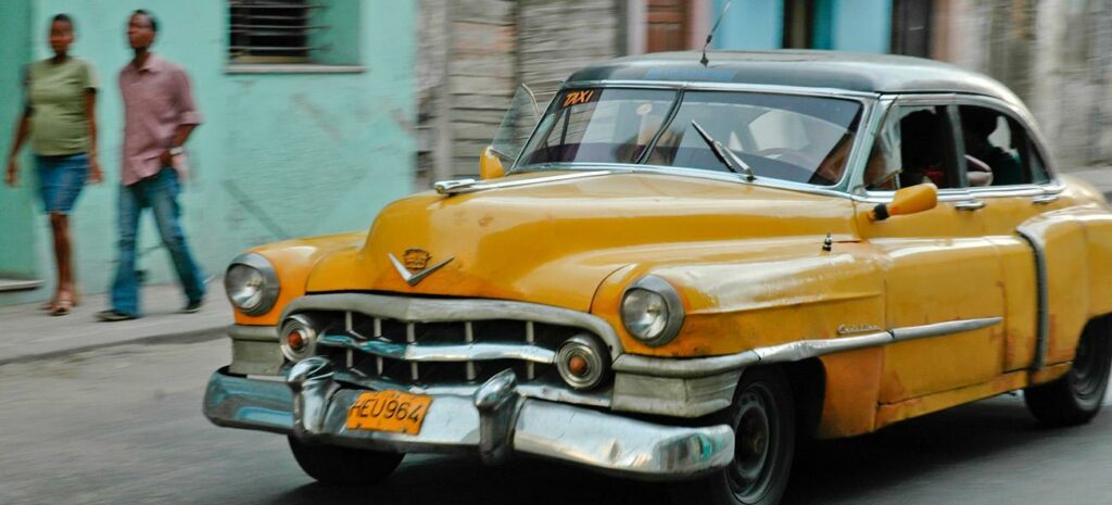 En gul bil körer nedför en gata i Kuba. (AI text)