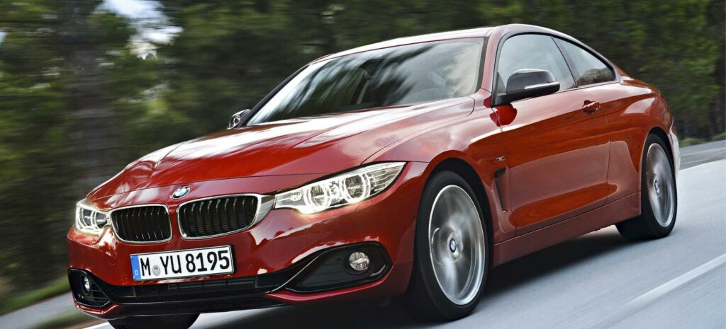 En BMW 4-serie coupé kör på en väg. (AI text)