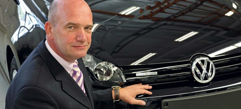 En man i kostym står bredvid en Volkswagen Golf. (AI text)