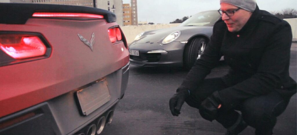 En man knäler ner bredvid en röd Chevrolet Corvette Stingray. (AI text)