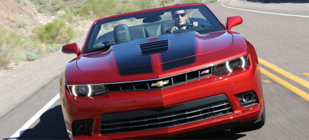 En röd Chevrolet Camaro kör nerför en bergsvidja. (AI text)