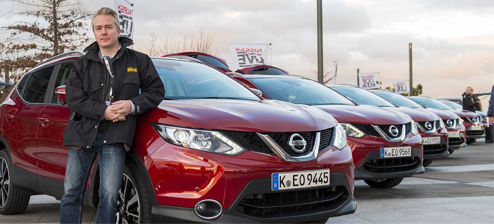 En man står bredvid en rad röda Nissan Qashqai-bilar. (AI text)