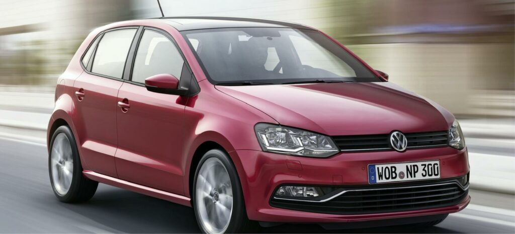 En röd Volkswagen Polo kör ner vägen. (AI text)