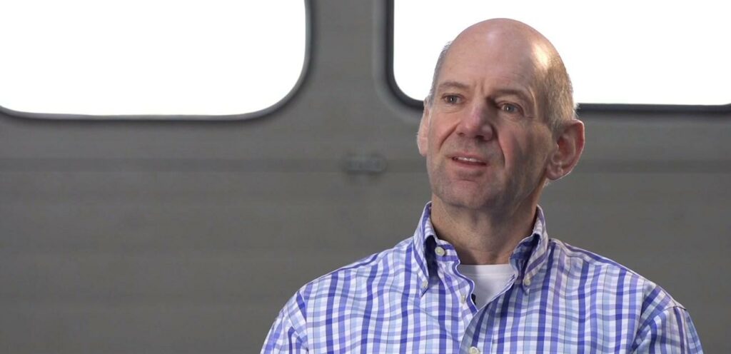 En man i ett tvärgående skjorta står framför ett fönster. (AI text)