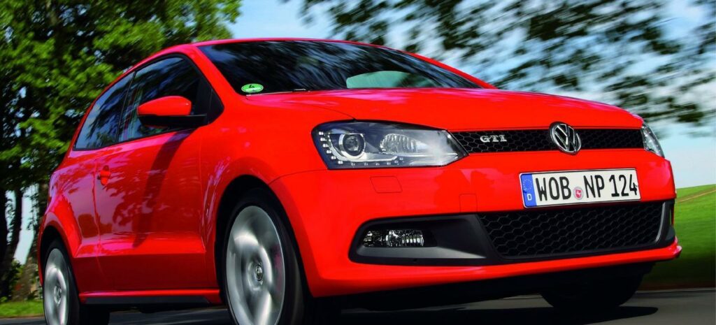 En röd Volkswagen Polo kör nerför en landsväg. (AI text)