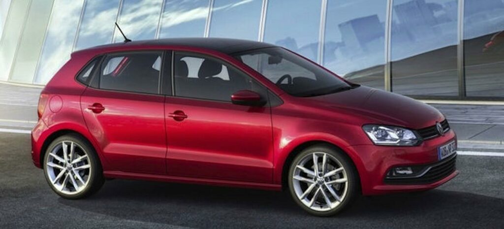 En röd Volkswagen Polo parkerad framför ett byggnad. (AI text)