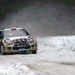 En rallybil körer nedför en snöig väg. (AI text)