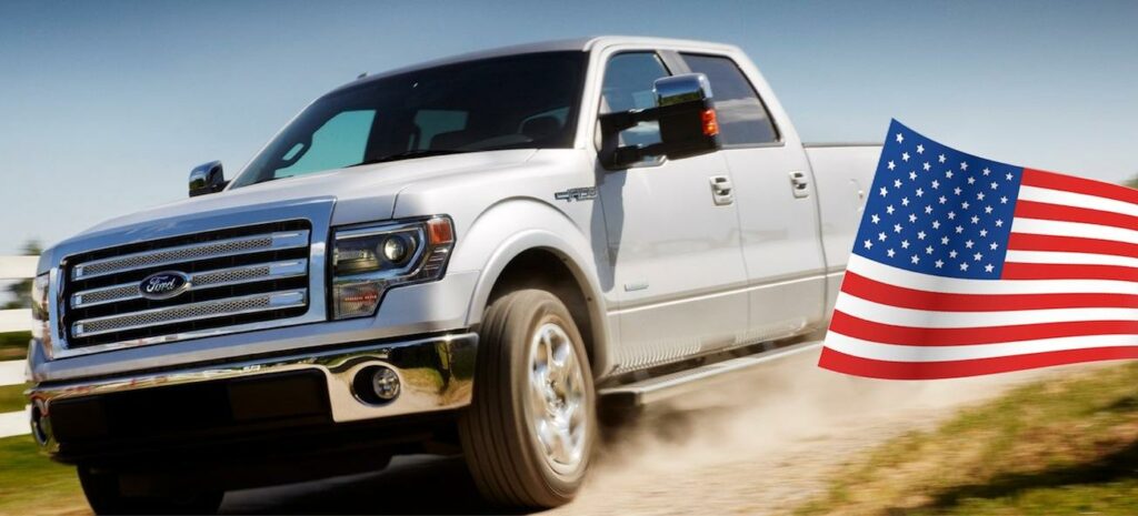 En vit lastbil kör nedför en grusväg medan en amerikansk flagga vajar i vinden. (AI text)