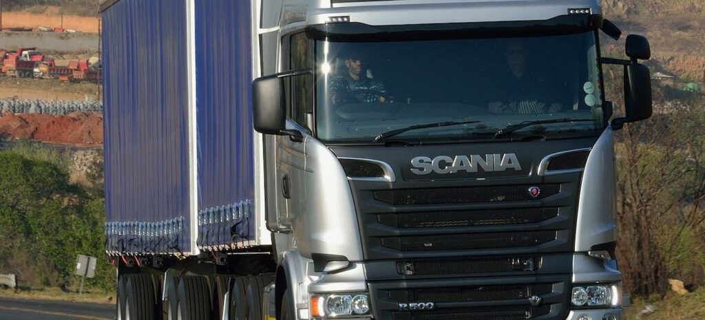 En Scania-lastbil kör nerför en landsväg. (AI text)