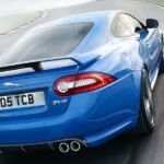En blå Jaguar XKR-sportsbil kör nedför en väg. (AI text)