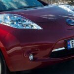 En röd Nissan Leaf elbil kör nerför en snöig väg. (AI text)