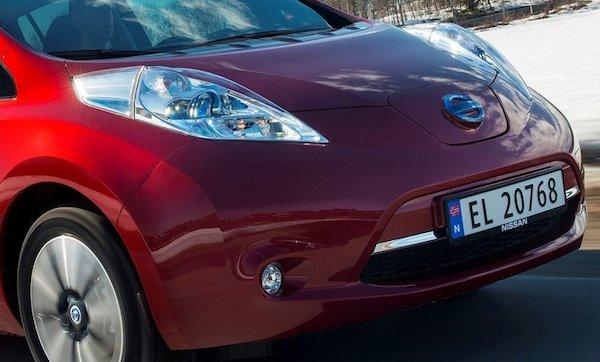En röd Nissan Leaf elbil kör nerför en snöig väg. (AI text)