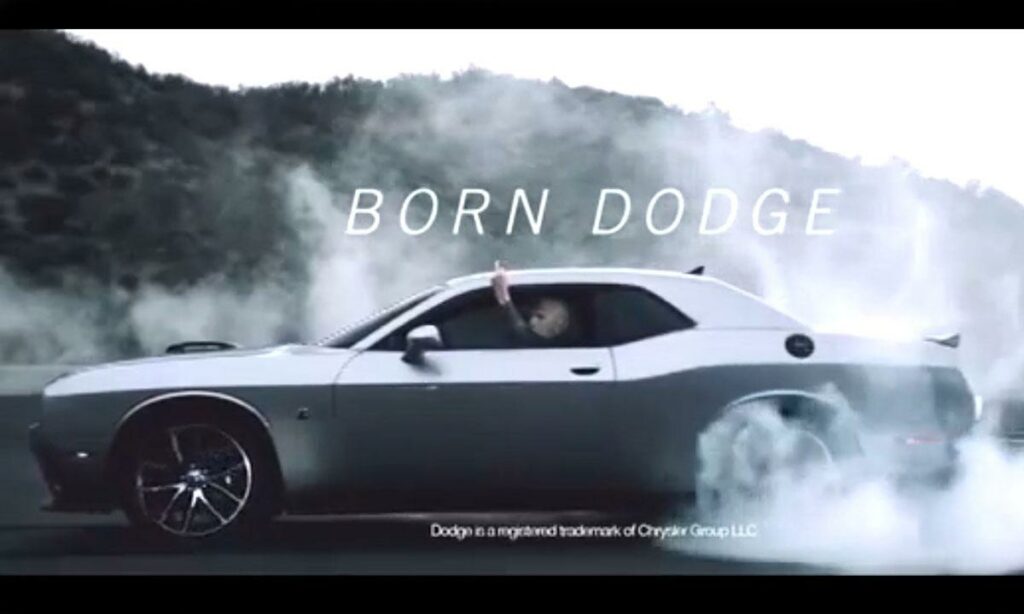 En man kör en Dodge Challenger med orden "born dodge" skrivna på bilen. (AI text)