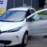 En man och en kvinna står bredvid en vit elbil. (AI text)