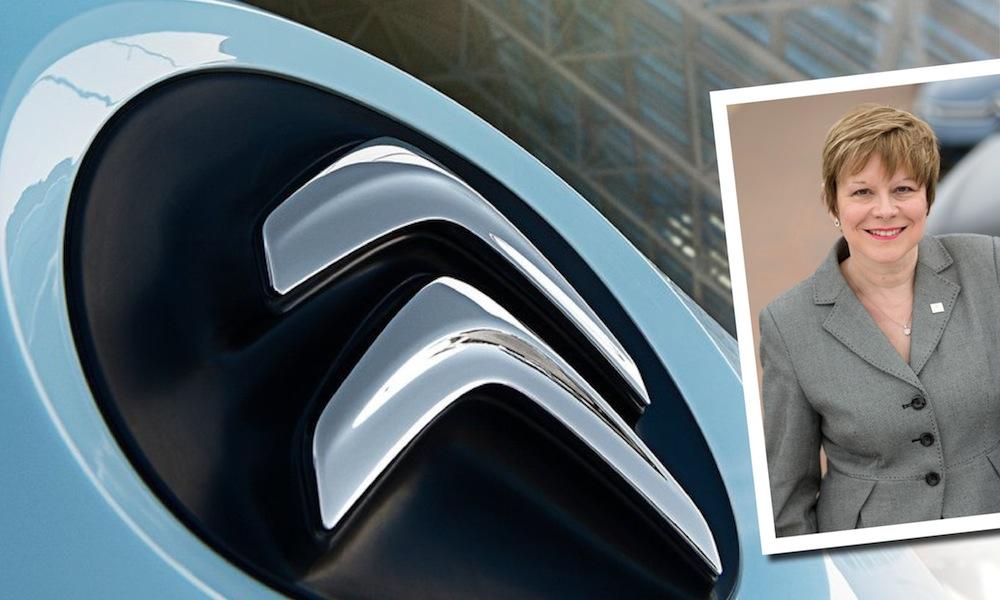 En kvinna i kostym och slips står bredvid en bil. (AI text)