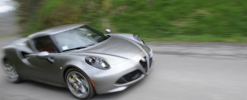 En silverfärgad Alfa Romeo sportbil kör nerför en bergsväg. (AI text)