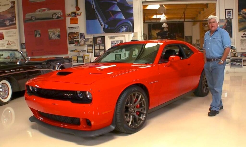 En man står bredvid en röd Dodge Challenger SRT. (AI text)