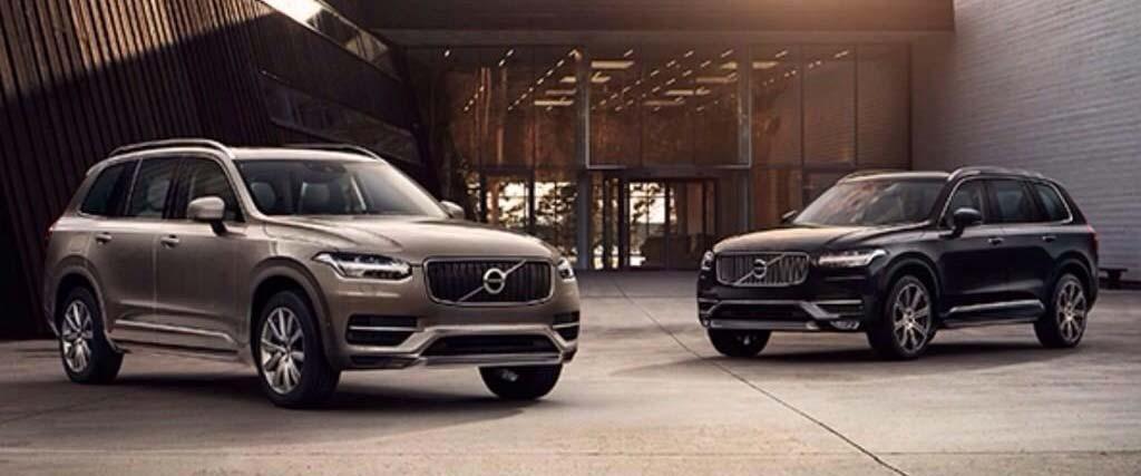 Två Volvo XC90 SUV:er parkerade framför ett byggnad. (AI text)