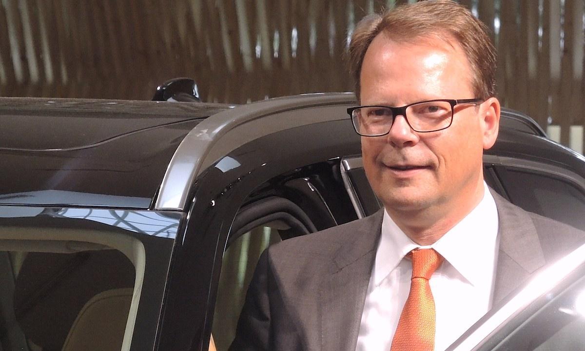 En man i kostym och slips står bredvid en bil. (AI text)