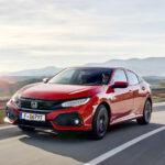 En röd Honda Civic kombi kör nedför en krökande väg. (AI text)