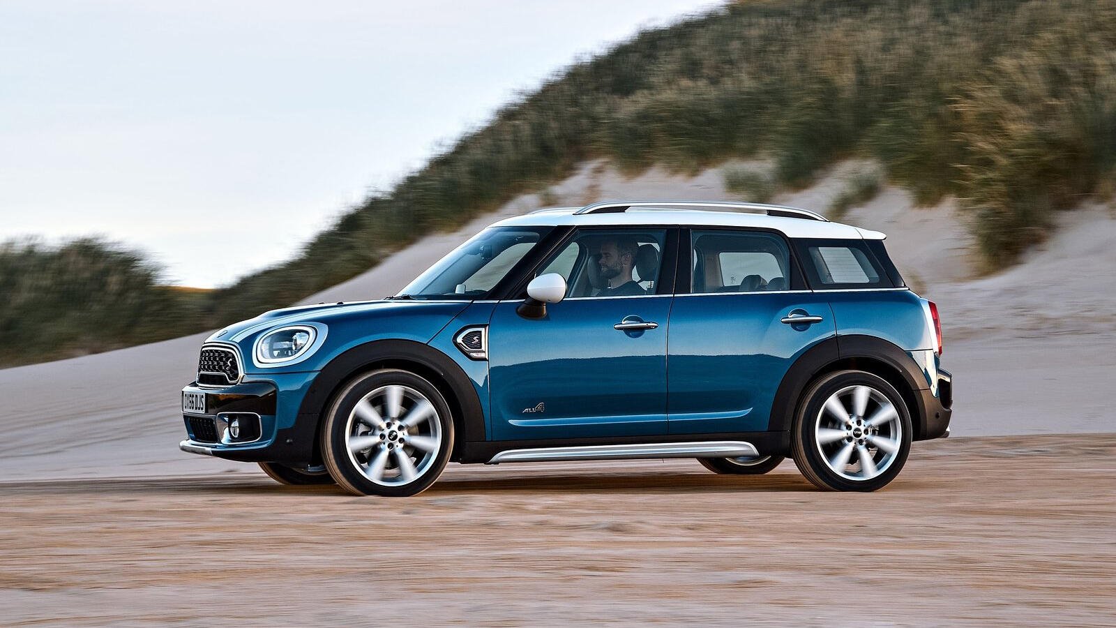 En blå Mini Countryman kör på en sandstrand. (AI text)