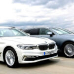 Två BMW X5 kör längs en landsväg. (AI text)