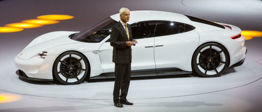 En man står bredvid en vit Porsche-bil. (AI text)