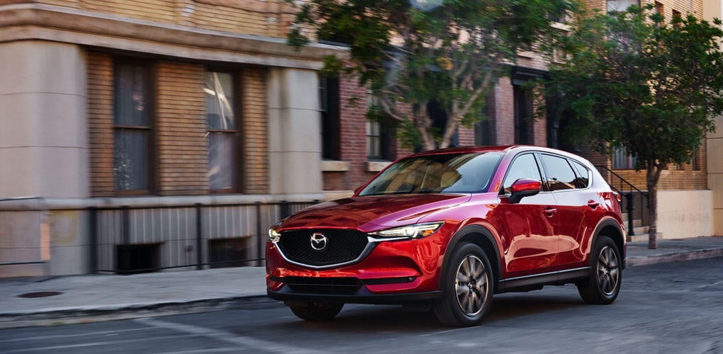 En röd Mazda CX-5 kör nedför en stadsgata. (AI text)