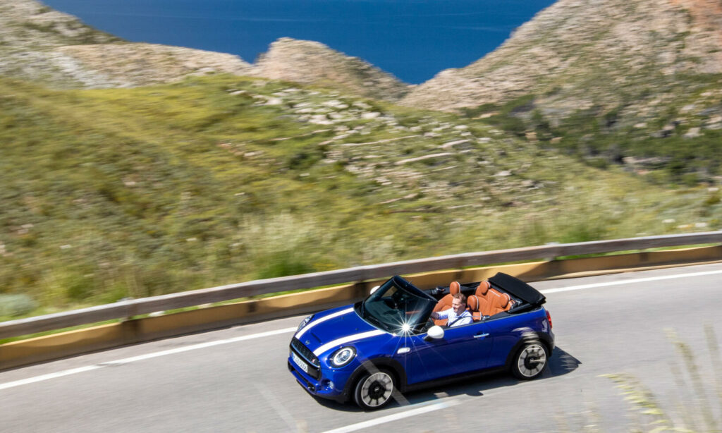 En blå Mini Cooper cabriolet kör nedför en bergsväg. (AI text)
