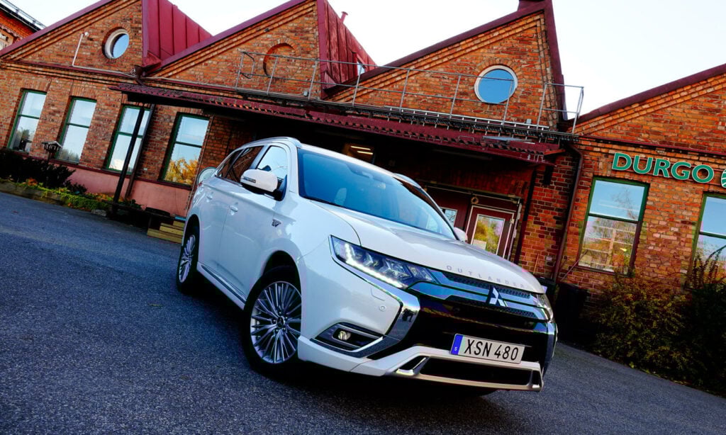 En vit bil står parkerad framför ett brunt tegelbyggnad. (AI text)