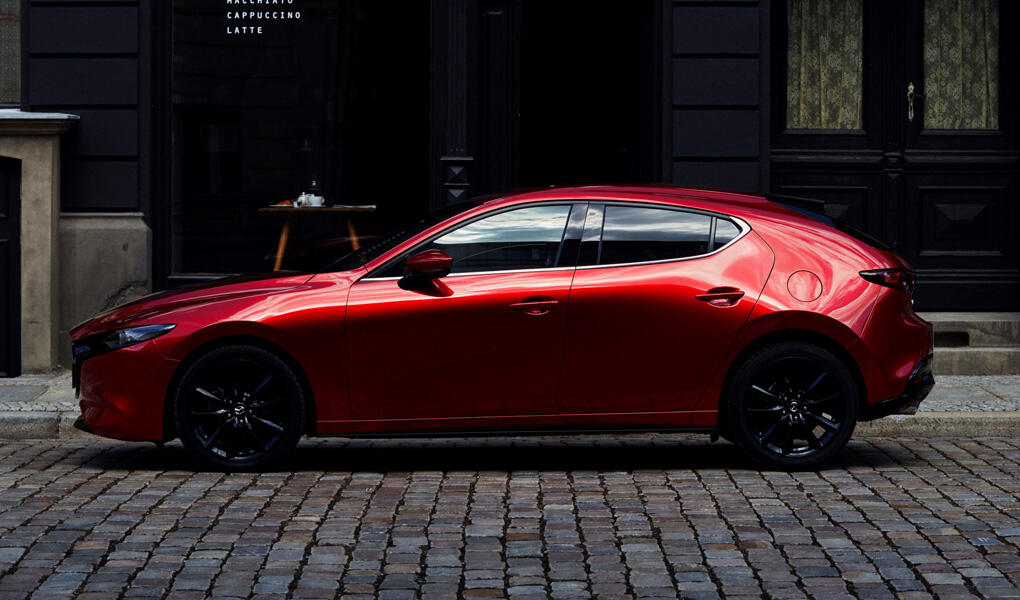En röd Mazda3 parkerad framför ett tegelbyggnad. (AI text)