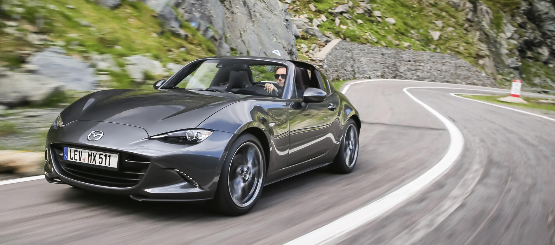 En Mazda MX5 roadster körer nedför en bergväg. (AI text)