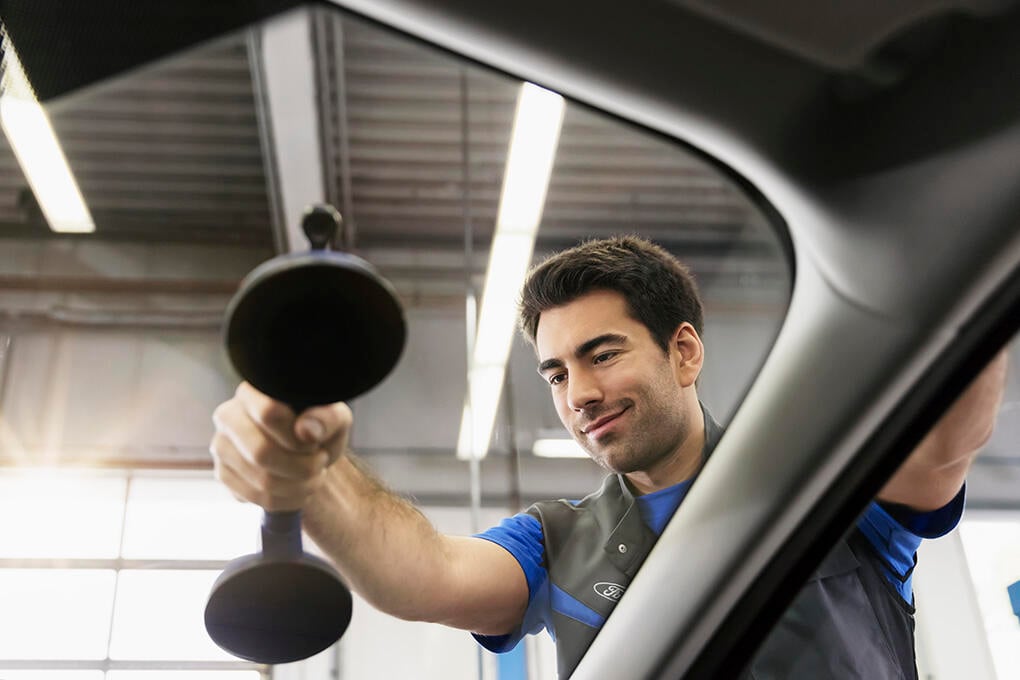 En mekaniker rengör vindrutan på en bil. (AI text)