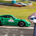 En man står bredvid en grön Porsche GT3. (AI text)