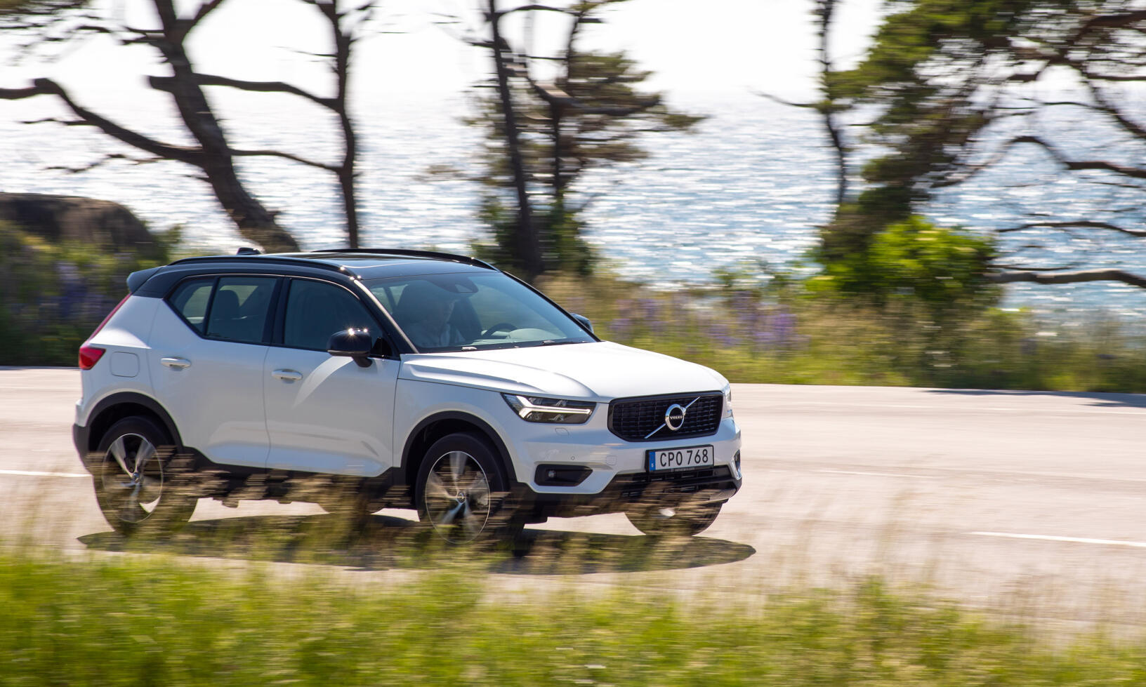 En vit Volvo XC90 SUV kör nerför en landsväg. (AI text)