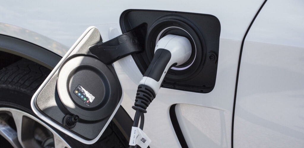 En vit bil är uppladdad i en elbilsladdare. (AI text)