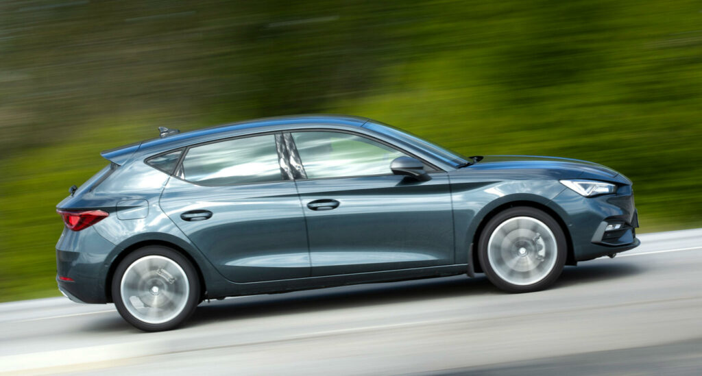 En blå hatchback kör nedför en väg. (AI text)