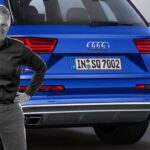 En man står bredvid en blå Audi Q7. (AI text)