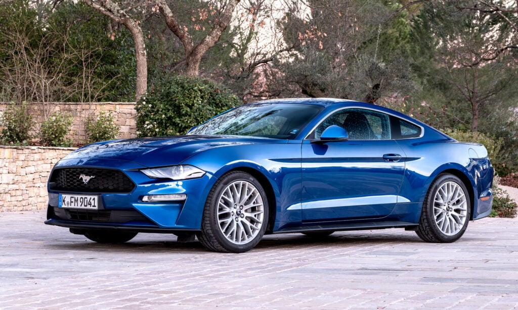 En blå Ford Mustang parkerad framför en stenmur. (AI text)