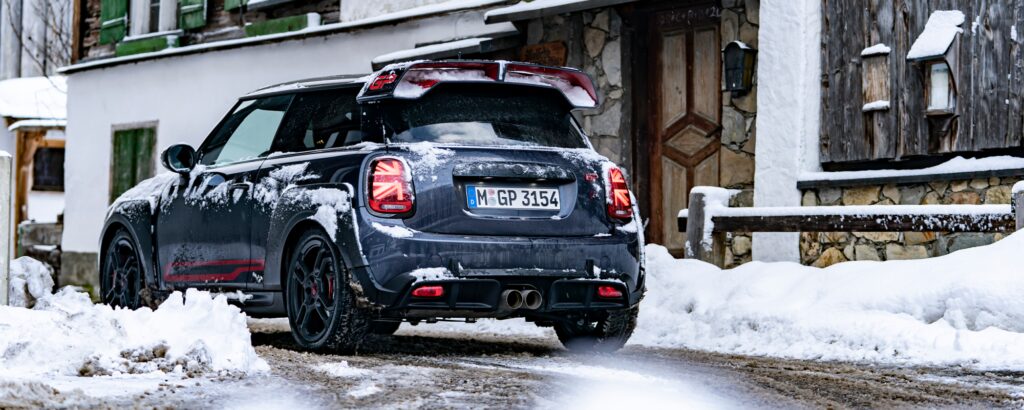 En Mini Cooper S kör genom ett snötäckt landskap längs en slingrig väg. (AI text)