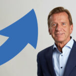 En man i kostym står framför en blå pil. (AI text)